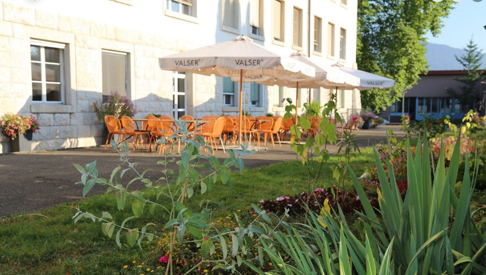 Terrasse fleurie avec parasols Valser devant le bâtiment historique de Courtemelon, au crépuscule